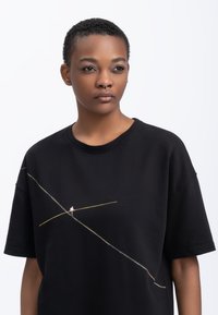 T-shirt noir oversize en coton, avec un design coloré brodé d'un funambule sur la poitrine. Manches courtes.