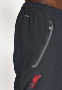 Schwarze Shorts mit einem elastischen Bund, seitlicher Reißverschlusstasche, silberfarbigen Akzenten und einem roten Liverpool FC-Logo am unteren Bein.