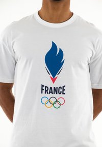Camiseta de algodón blanca con un logotipo de llama azul encima de la palabra "FRANCIA" en negrita color marino, con los aros olímpicos en múltiples colores debajo.