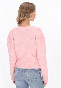 Rozā pūkaina džemperis ar ribinātu apakšmalu un garām piedurknēm, ar apaļu kaklu, mīkstu tekstūru un nedaudz saīsinātu dizainu. Valkāts ar džinsu biksēm.