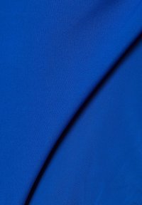 Slen, vibrerande blått tyg med en lätt lyster; texturerat ribbat mönster med överlappande veck som skapar visuell djup.