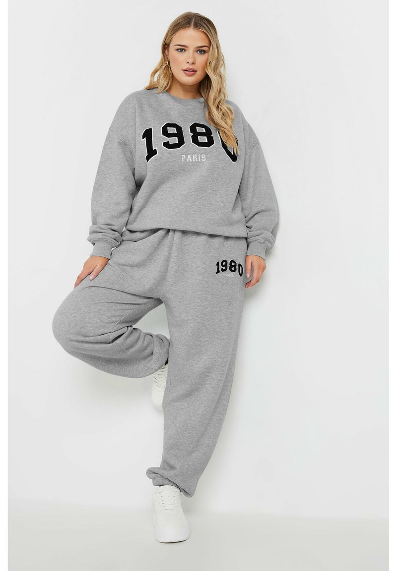 Conjunto de sudadera y pantalones de chándal grises con un gráfico negro de "1980" y el texto "PARÍS", hecho de una suave mezcla de algodón, con un corte relajado.