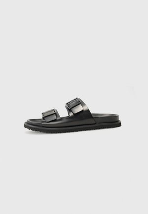 Czarne klapki typu slip-on z dwiema regulowanymi klamrami, wykonane z gładkiego materiału syntetycznego, z teksturowaną podeszwą zapewniającą przyczepność.