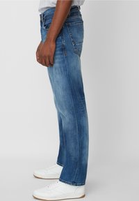 Jeans de mezclilla azul claro con corte recto, textura desgastada y cinco bolsillos. Llevados con zapatillas blancas.