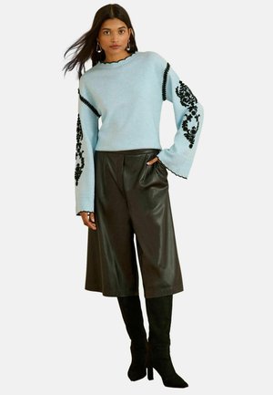 Light blue sweater with black floral embroidery on sleeves, paired with black faux leather culottes and knee-high black boots.