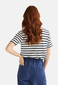 T-shirt à manches courtes rayé en gris clair avec des rayures bleu marine, associé à un pantalon élastique à taille haute bleu foncé avec deux poches arrière.