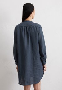 Donkerblauwe linnen shirtjurk met lange mouwen, geplooid detail aan de achterkant en een lichte high-low zoom, met een kraag en knoopmanchetten.