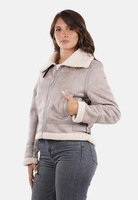 Giacca in suede grigio con colletto e polsini in pelliccia sintetica color crema, dotata di chiusura con zip, tasche laterali e un accento in cintura in vita.