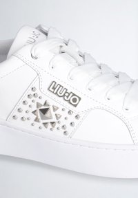 Sneaker bianca con tomaia in pelle liscia, punta tonda e suola piatta bianca. Decorata con borchie argento e un accento a forma di diamante.
