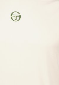 Chemise polo blanche en tissu texturé, dotée d'un logo circulaire vert en haut à gauche. Design simple et classique.