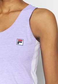 Lila tílko s hladkou texturou, s bílým bočním panelem a malým logem Fila v červené a černé barvě. Bez rukávů.