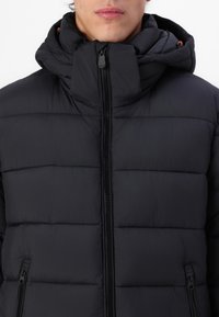 Zwarte pufferjack met een hoge kraag en ritssluiting. Bevat horizontale stiksels, zijzakken en een verstelbare capuchon met oranje accenten.