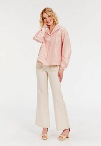 Blouse rayée à manches courtes en rose clair et blanc, avec un col pointu. Associée à un jean fluide écru et des talons compensés beiges.