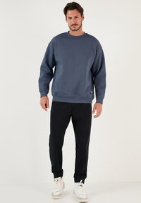 Felpa blu navy con scollatura a girocollo e polsini a costine, abbinata a pantaloni della tuta neri a gamba affusolata e sneakers bianche. Tessuto morbido e testurizzato.