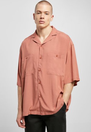 Chemise à manches courtes, de couleur corail, boutonnée, fabriquée dans un tissu doux, présentant deux poches avant et un col classique. Couleur ample et design léger.