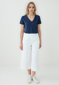 Granatowy t-shirt z dekoltem w serek w zestawieniu z białymi szerokimi spodniami i białymi sneakersami; gładki materiał, klasyczny krój i minimalistyczny design.