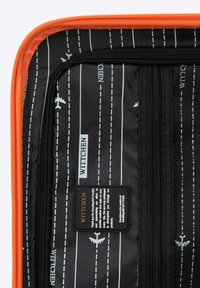 Interno di una valigia rigida con rivestimento nero, motivo aereo bianco e linea tratteggiata, presenta una tasca con zip e etichetta WITTCHEN. Rifiniture arancioni.