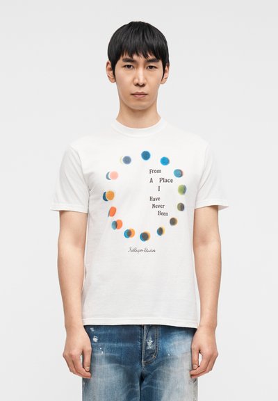 Λευκό βαμβακερό μπλουζάκι με κυκλικό μοτίβο από πολύχρωμες κουκκίδες και κείμενο «From A Place I Have Never Been» σε μαύρο, άνετη εφαρμογή, κοντά μανίκια.