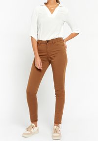 Brown skinny pants made of cotton blend fabric, featuring a high waist, front pockets, and a smooth texture. Paired with a white v-neck blouse.