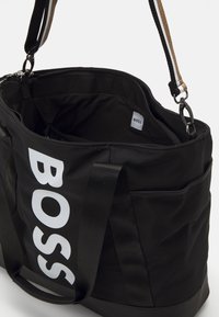 Fekete nejlon bevásárlótáska nagy fehér "BOSS" logóval, dupla fogantyúkkal és állítható vállpánttal. A belső tér több rekesszel rendelkezik.