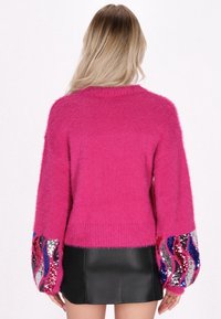 Fluffy roze trui met lange mouwen, voorzien van pailletten golfpatronen in zilver, rood en blauw. Afgewerkt met een geribbelde zoom.