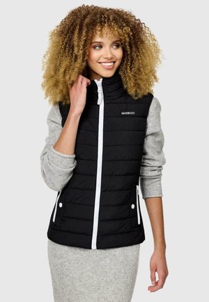Black puffer vest with a high collar, white zipper, and side pockets. Worn over a gray long-sleeve top, featuring quilted texture.