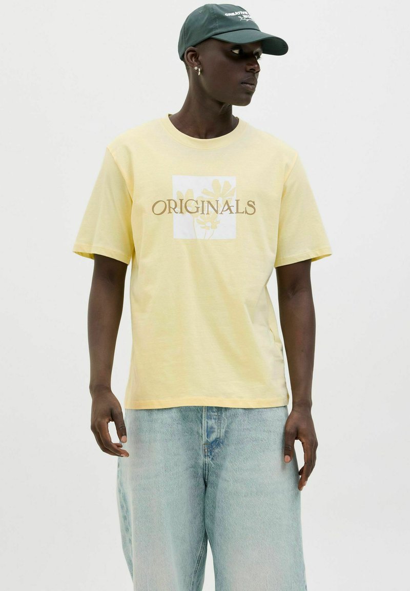 Yellow cotton t-shirt with short sleeves featuring "ORIGINALS" text and floral design in a square, paired with light blue denim shorts.