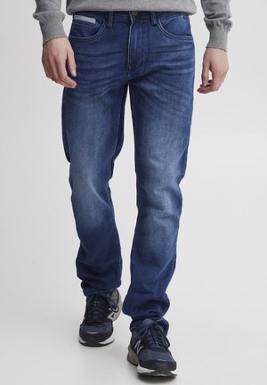 Blå denimjeans med rett passform, fem lommer, og lette slitasjedetaljer. Brukt med svarte og grå joggesko.
