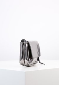 Borsa a tracolla grigia metallizzata con superficie liscia e lucida. Presenta un risvolto, un dettaglio intrecciato nella parte superiore e una chiusura con cordoncino.
