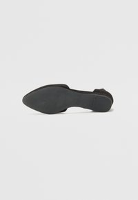 Zapato de tacón negro de ante con punta afilada y tacón bajo. La suela es de goma texturizada para mayor adherencia, con un branding mínimo.