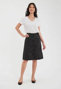 Jupe noire à boutonnières avec poches avant et design à longueur genou, associée à un T-shirt blanc à col en V et des chaussures marron et noires.