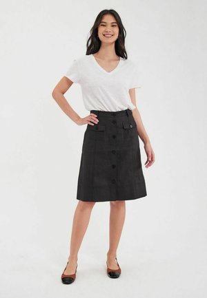 Jupe noire à boutonnières avec poches avant et design à longueur genou, associée à un T-shirt blanc à col en V et des chaussures marron et noires.