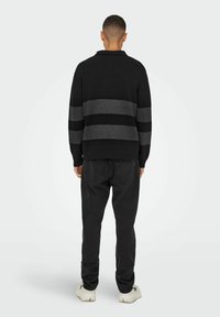 Schwarzer Pullover mit grauen horizontalen Streifen, gestrickte Textur, mit Kragen; kombiniert mit schwarzen Hosen und hellen Sneakers. Rückansicht.