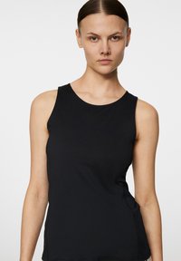 Svart ärmlös topp i mjuk tyg, med rund halsringning och diskret logotyp på framsidan. Slim fit med rena sömmar.