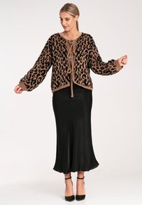 Leopardenmuster-Cardigan in Beige und Schwarz, aus gestricktem Material, mit einem cropped Design, langen Ärmeln und einer Bindeschleife vorne. Kombiniert mit einem schwarzen Satins Rock.