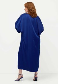 Royal blue satiinimaksimekko, jossa on ylisuuria hihoja, virtaava siluetti ja sivuaukot. Yhdistetty sinisiin hihnakenkiin.