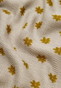 Tkanina tkana w wzór rybiej ości w jasnym beżu, z rozsianymi żółtymi motywami kwiatowymi. Miękka w dotyku z delikatnym połyskiem.