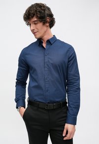 Tengerészkék gombos ing texturált mintával, karcsúsított szabású, kenhető gallérral, hosszú ujjú, fekete nadrággal és fekete övvel párosítva.