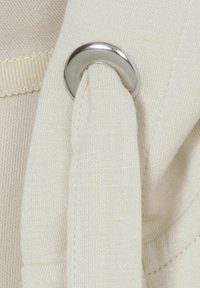 Cremfarbene Stoff mit glatter Textur, versehen mit einem metallischen silbernen Ösen und einer Stoffschlaufe. Dezente Rippendetail entlang des Randes.