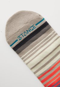 Bunter gestreifter Socken aus Stoff, mit grauen, beigen, marineblauen und korallenfarbenen Tönen, und "STANCE" in Türkis auf dem Bündchen gestrickt.