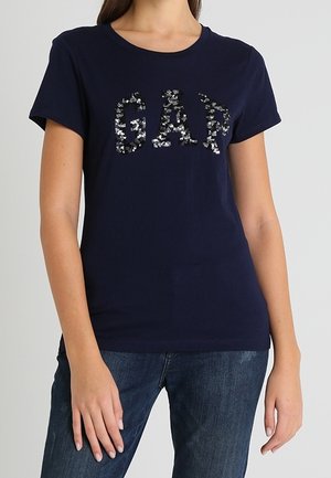 Navyblaues Baumwoll-T-Shirt mit kurzen Ärmeln, das mit einem glitzernden "GAP"-Logo in Silber verziert ist. Der Schnitt ist lässig und wird mit Jeans aus Denim kombiniert.