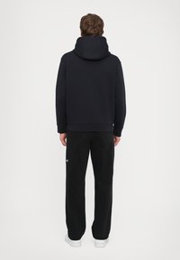 Marineblaues Kapuzensweatshirt mit lockerer Passform, gerippten Bündchen und Saum. Getragen mit schwarzen geraden Jeans und weißen Sneakers. Minimale Branding sichtbar.