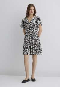 Schwarzes und weißes gemustertes Kleid mit V-Ausschnitt, kurzen, schwingenden Ärmeln und gerafftem Taillenbereich, ausgestattet mit einem gestuften Rock und leichtem Stoff.