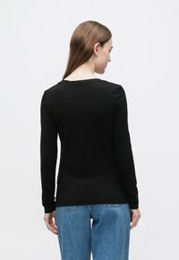 Črna majica z dolgimi rokavi iz gladkega materiala, okrogel izrez in oprijeti rokavi. Oblečena z svetlo modrimi kavbojkami.
