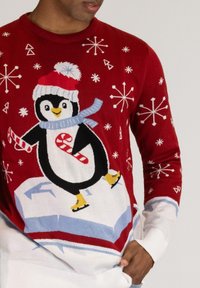 Red knit sweater featuring a penguin graphic wearing a hat and scarf, with snowflakes and candy canes pattern. Ribbed white cuffs and hem.