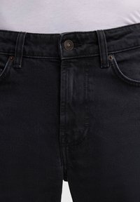 Schwarze Denim-Jeans mit einem Fünf-Taschen-Design, Kupferknopfverschluss und sichtbaren Nähten. Der Stoff hat eine glatte Textur.