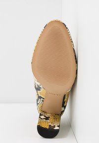 Chaussure à talon à motif serpentin noir, jaune et blanc avec une surface texturée et une semelle en caoutchouc flexible. Base du talon plate avec un motif strié.