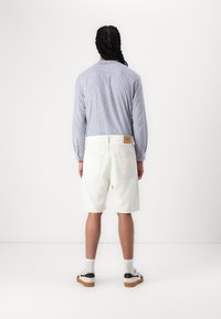 Stribet blå langærmet skjorte, lyse shorts, hvide sokker og sneakers. Har en baglomme på shortsene og knapdetaljer på skjorten.