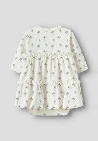 Hvit kjole med lange ermer, blomsterprint i grått. Har rysjekant nederst, rund hals og trykknapper i bunnen for enkel påkledning.