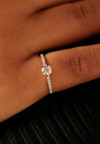 Diamond engagement ring featuring a round center stone, a delicate band with small accent diamonds, set in white gold.
